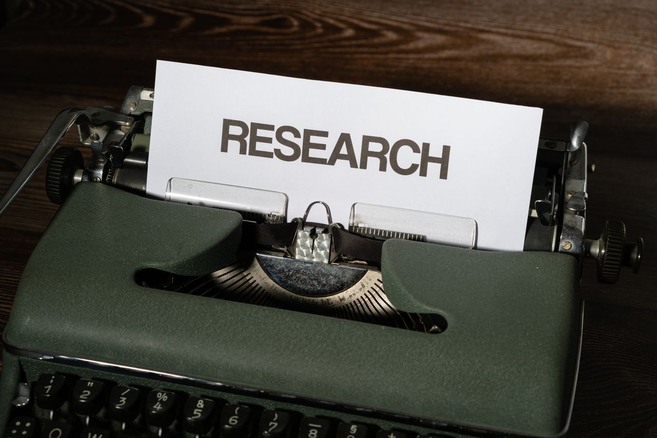 about-01 Close-up of a vintage typewriter with a paper labeled 'Research' inserted, on a wooden surface.