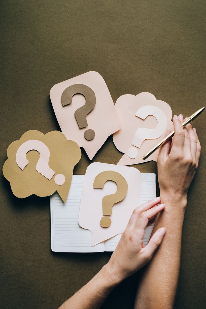 gallery-5 Hands holding pen next to paper question marks on notebook, symbolizing inquiry and creativity.